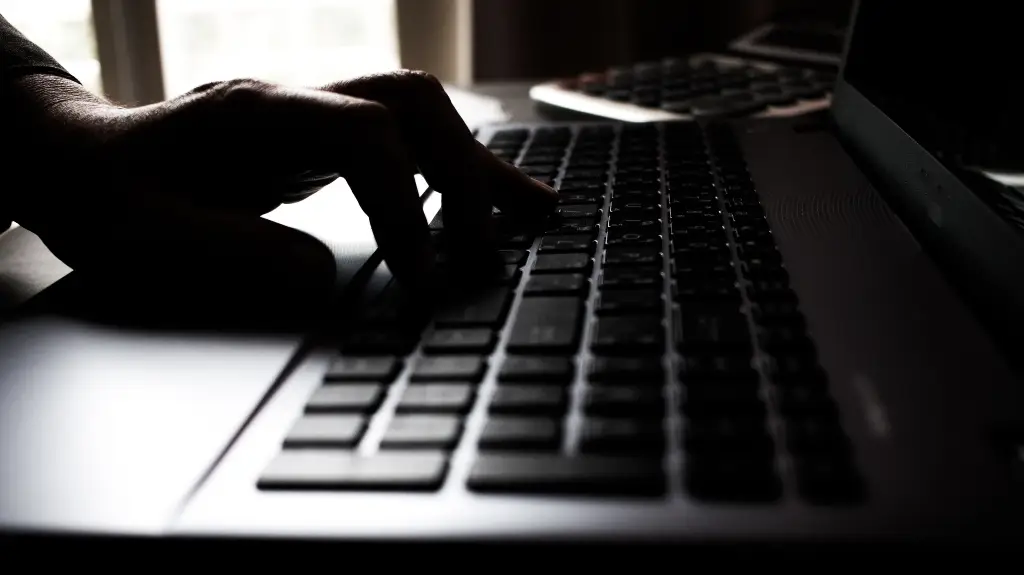 Close-up of a person’s hand typing on a black laptop keyboard in low light.
