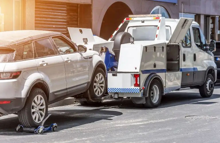 White tow truck loading a silver SUV on an urban street during daytime.