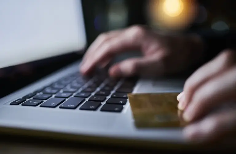 Close-up of hands holding a gold credit card and typing on a laptop keyboard.